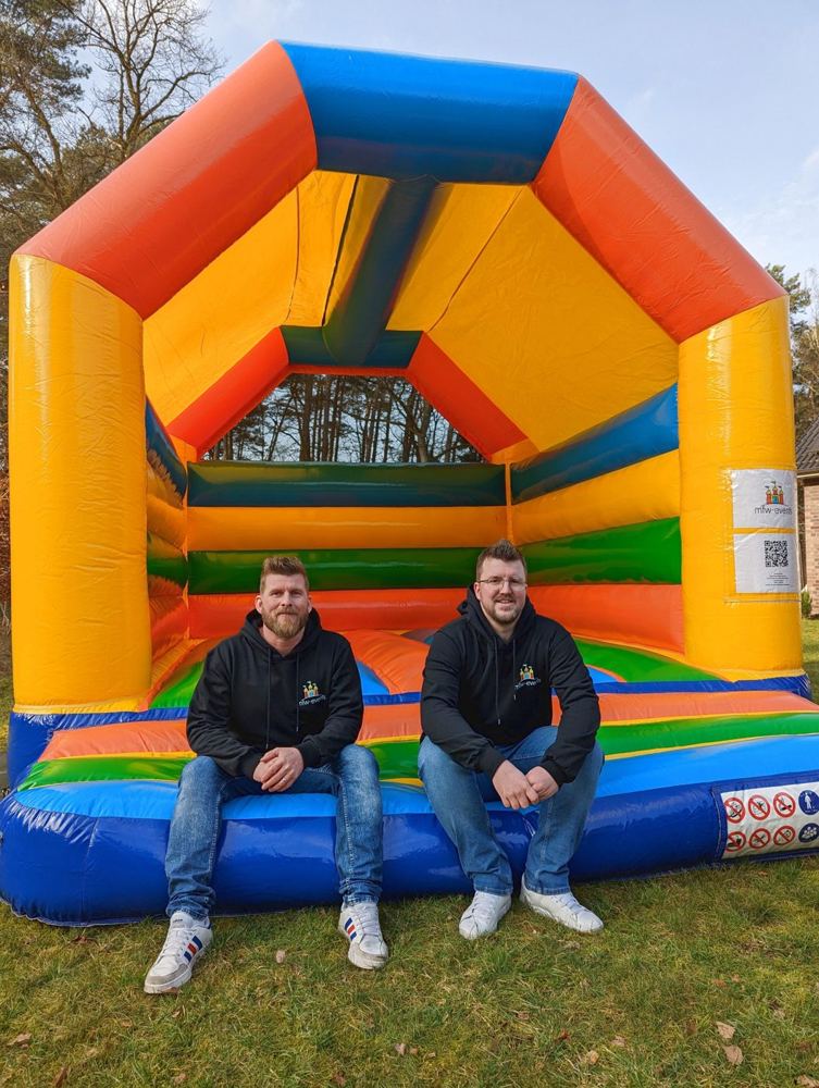 Michael und Fabian Wennmann sitzen vor einer bunten Hüpfburg